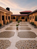 Un patio con piso de baldosas, plantas en macetas y un edificio de techo rojo.