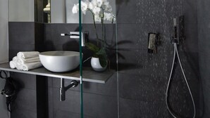 Ein modernes Badezimmer mit großem Spiegel, weißem Waschbecken, einer Dusche und einem Topf mit einer Orchidee.