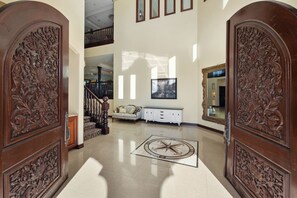 Una entrada imponente con puertas de madera ornamentadas, una escalera central y una consola blanca.