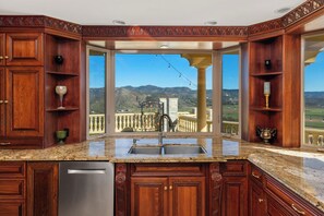 Una cocina con armarios de madera, lavavajillas de acero inoxidable y vistas a la montaña a través de un amplio ventanal.