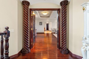Un pasillo con piso de madera, un candelabro y una puerta blanca al final.
