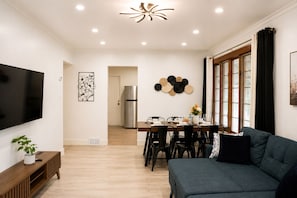 A modern living room with a flat-screen TV, a dining area with a wooden table and chairs, and a grey sofa. - Vanta Villa - 2BR • 1 Bath • 4 Min to Niagara Falls (Niagara Falls)