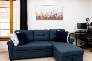 Ein modulares Sofa mit dunkelblauem Stoff, zwei Zierkissen, ein gerahmtes Blumenbild an der Wand, ein Computertisch mit Bildschirm und eine Windmühlendekoration.