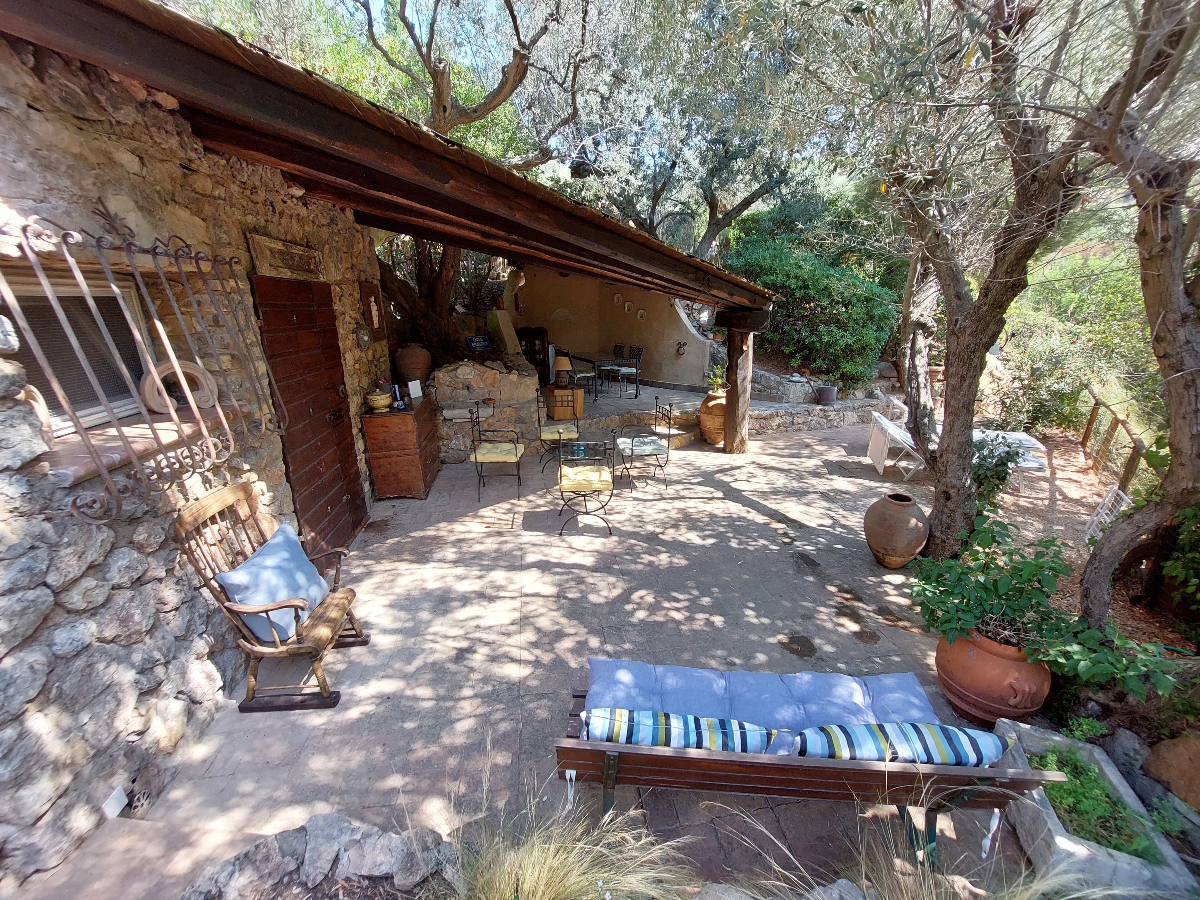An outdoor patio area with stone walls, wooden furniture, and potted plants.