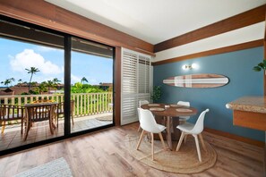 Ein Zimmer mit Esstisch, Stühlen, einer Surfbrett-Dekoration und Blick auf einen Balkon mit Gartenmöbeln.