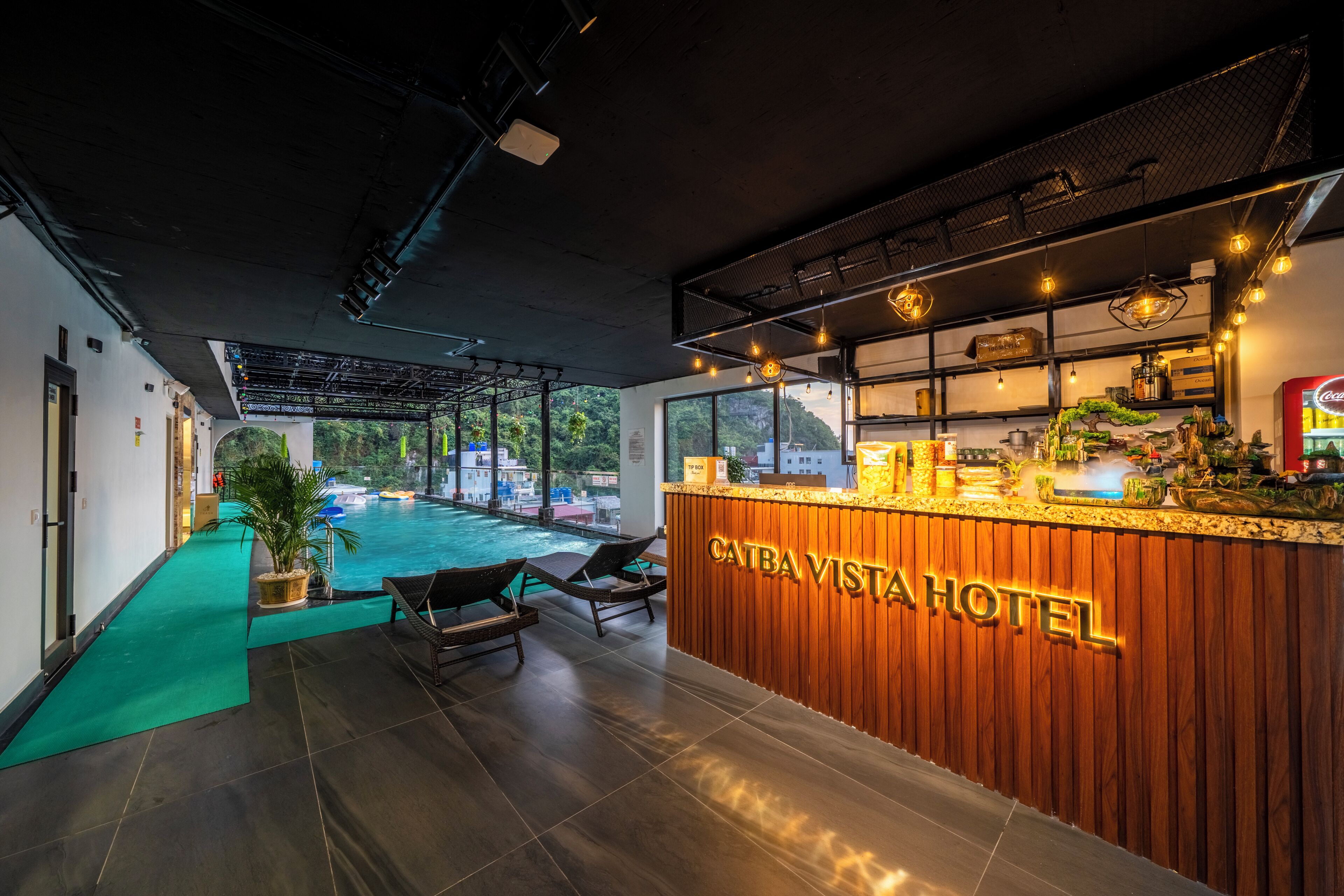 A reception area with a wooden counter, lounge chairs, and a view of an outdoor swimming pool.