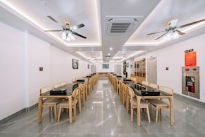 A conference room with long tables, chairs, ceiling fans, and a fire extinguisher.