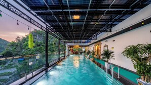 An indoor swimming pool with a glass barrier, surrounded by greenery and a mountainous backdrop. - Catba Vista Hotel (Hai Phong)