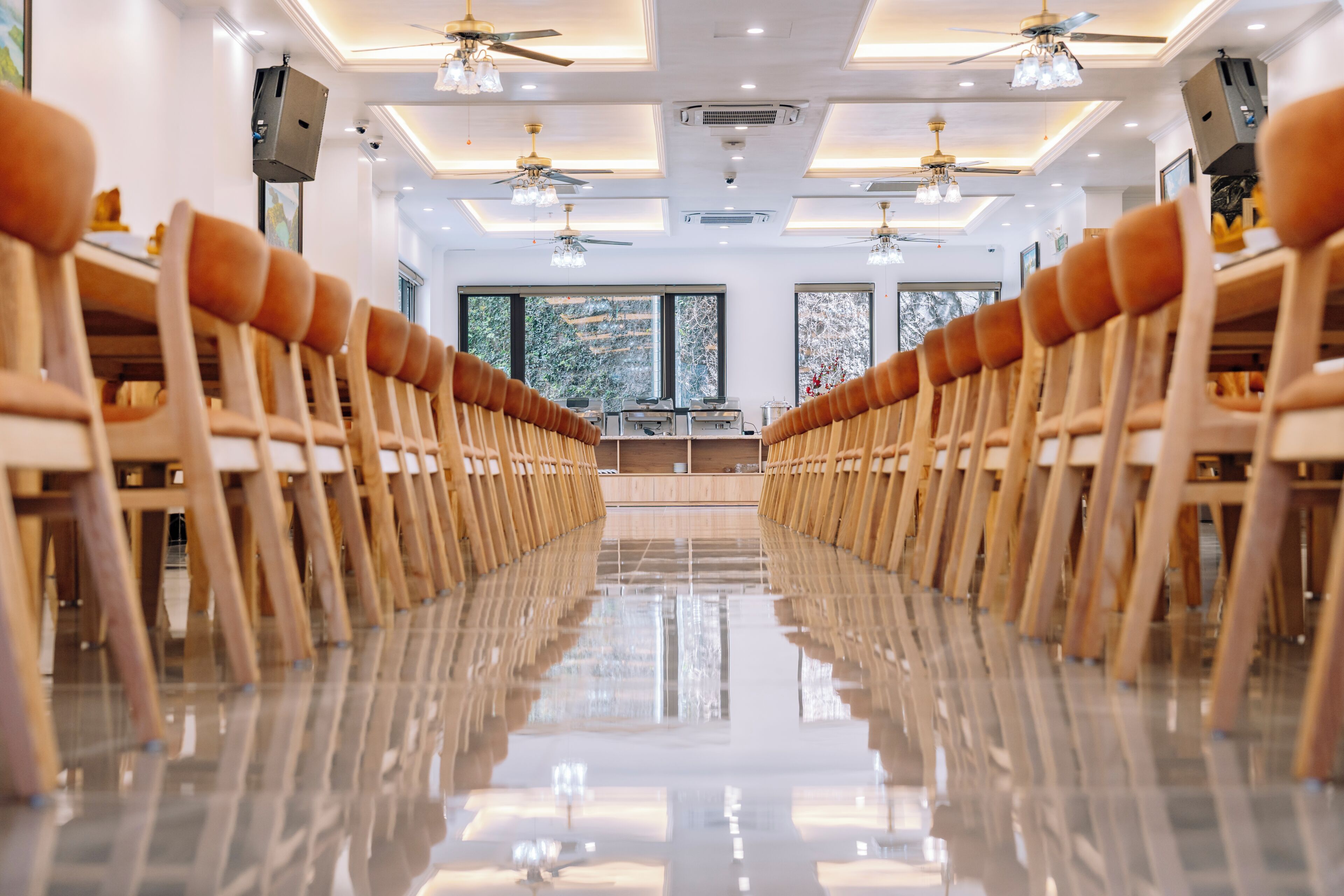 A long, reflective aisle with rows of wooden chairs and ceiling fans.