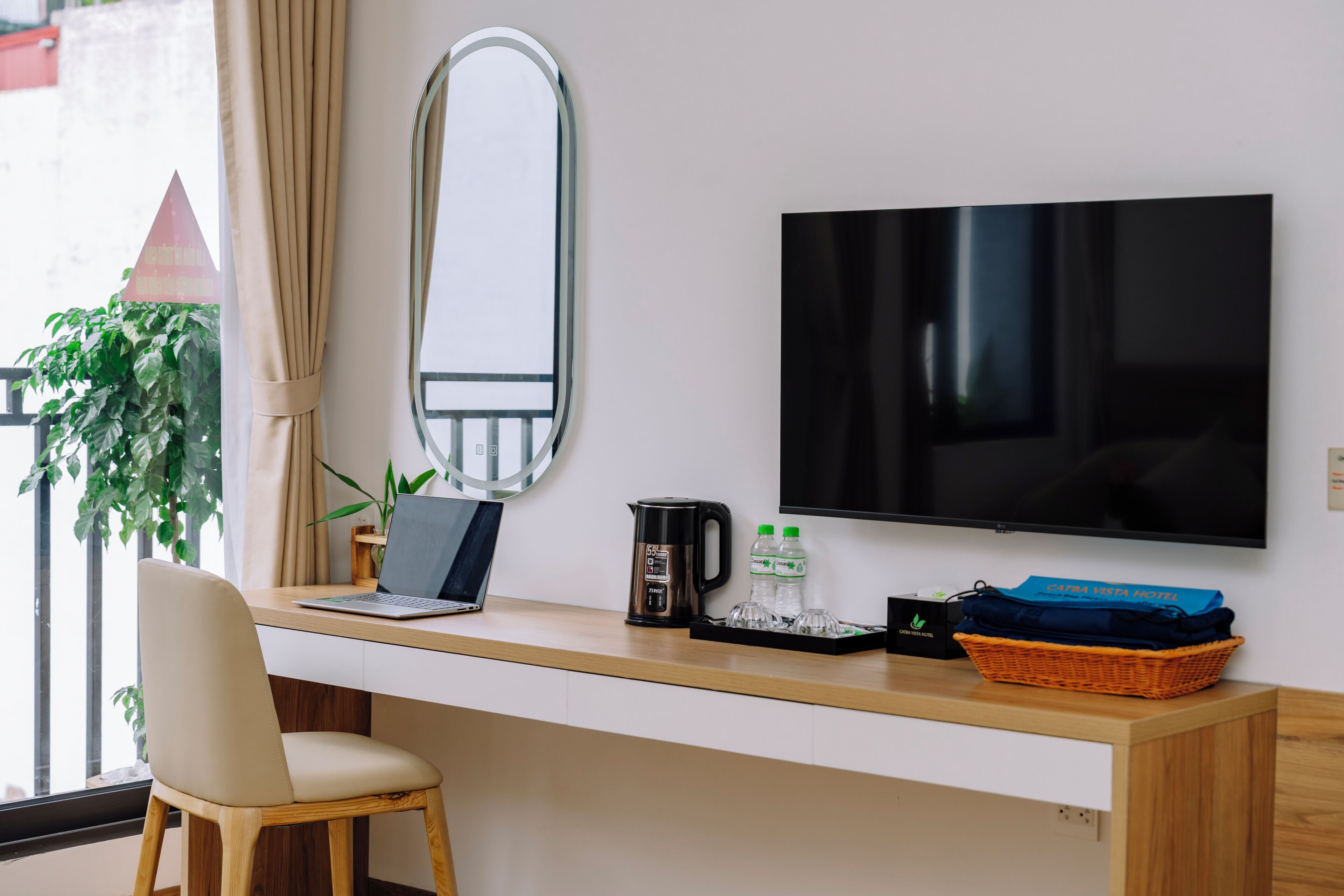 A modern hotel room with a wooden desk, a laptop, a coffee maker, and a flat-screen TV.