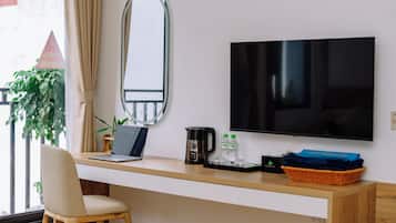 A modern hotel room with a wooden desk, a laptop, a coffee maker, and a flat-screen TV.