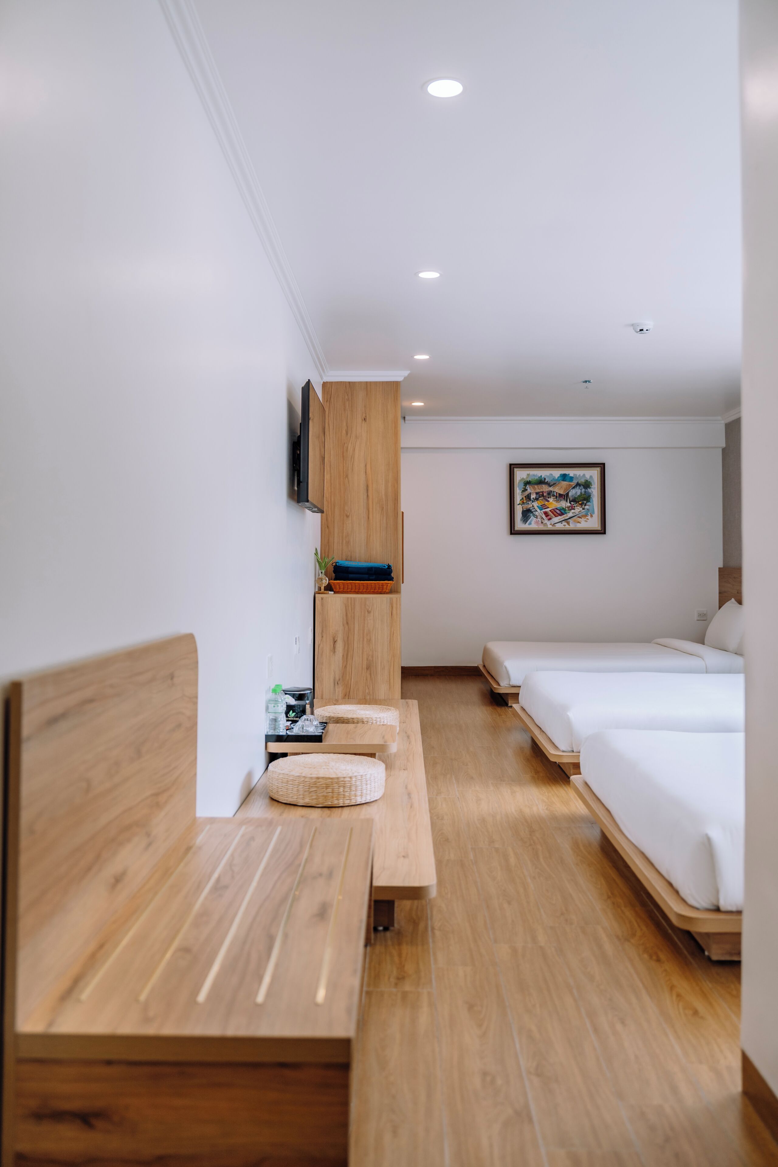Ein Hotelzimmer mit einer hölzernen Bank, zwei Betten, einem Flachbildfernseher, einem Gemälde und einer Deckenleuchte.