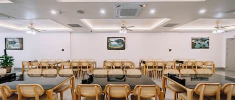 A conference room with a large table surrounded by chairs, ceiling fans, and artwork on the walls.