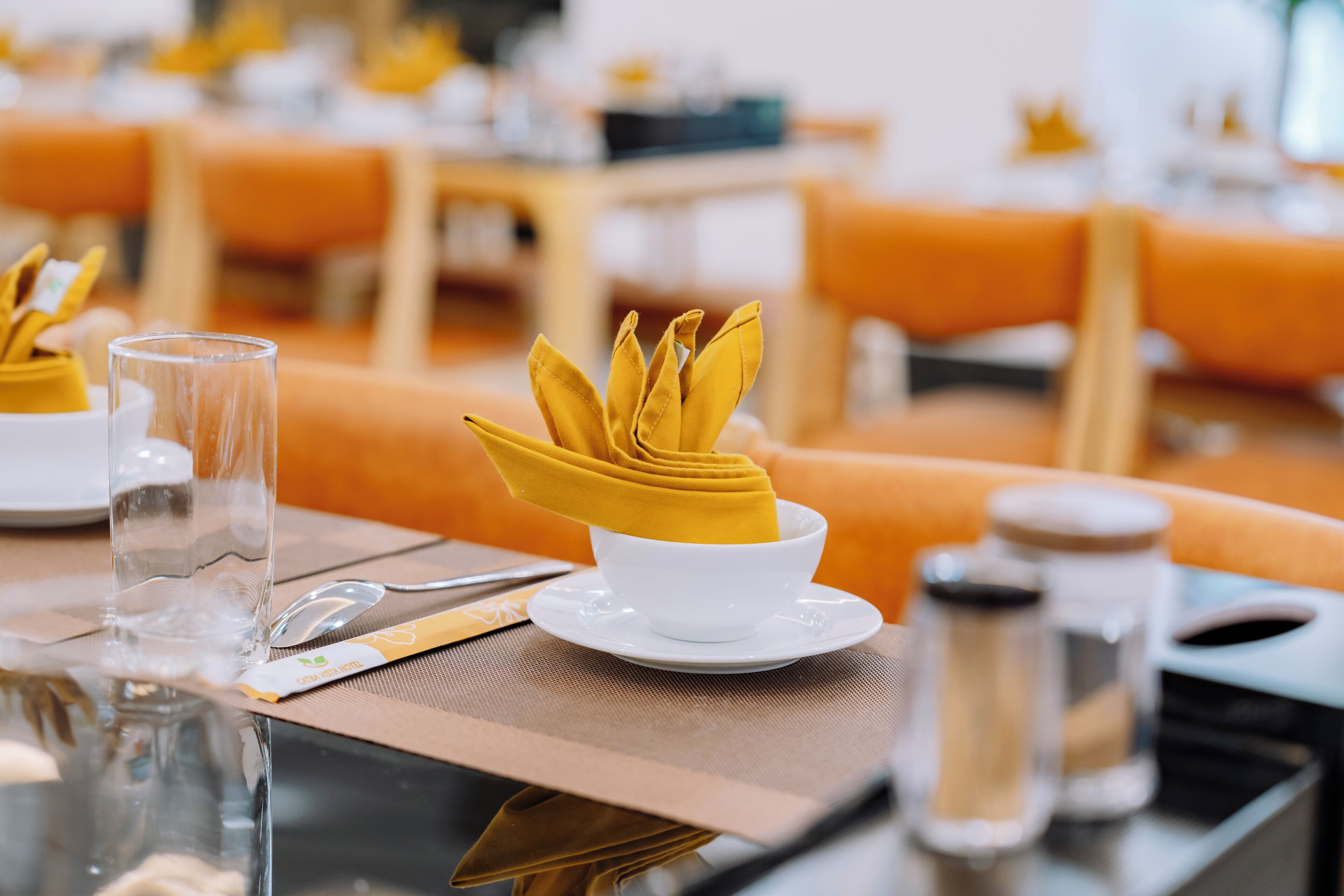 A dining table set with a clear glass, a folded napkin, a spoon, and a white bowl.