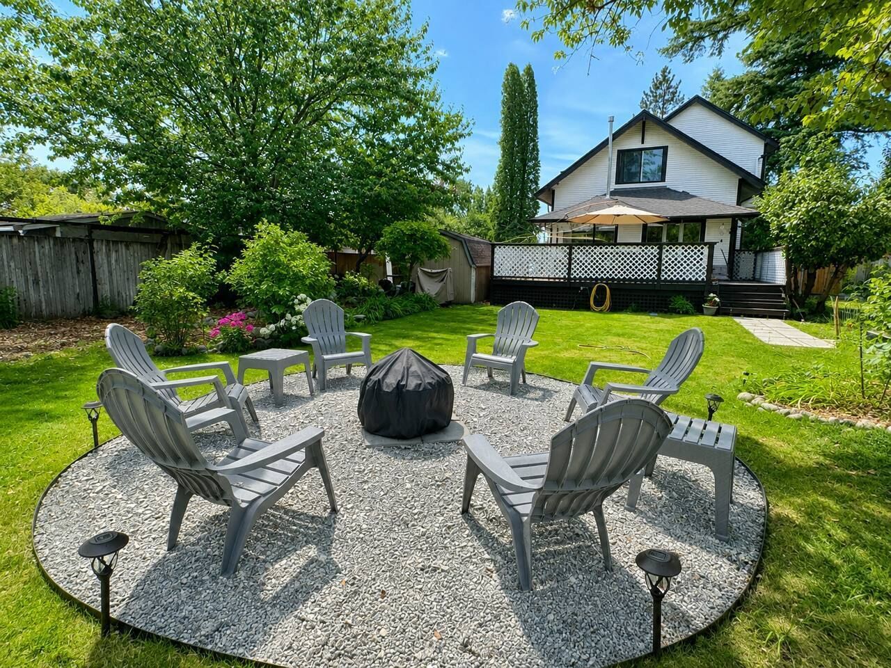 A circular outdoor seating area with Adirondack chairs and a fire pit, surrounded by a gravel patio.