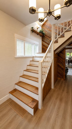 A staircase with wooden steps and white railings, leading to a landing with a view of a wooden wall and a window with blinds. - Charming Farmhouse with Hot Tub, Fire Pit & Mountain Views near Wallace Falls (Gold Bar)