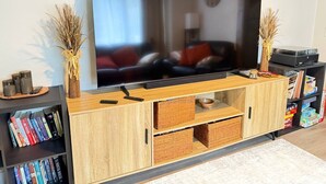 A modern living room with a flat-screen TV on a wooden TV stand, surrounded by bookshelves and decorative items. - Mountain Cabin With Hot Tub & Fire Pit, Wallace Falls & Stevens Pass (Gold Bar)