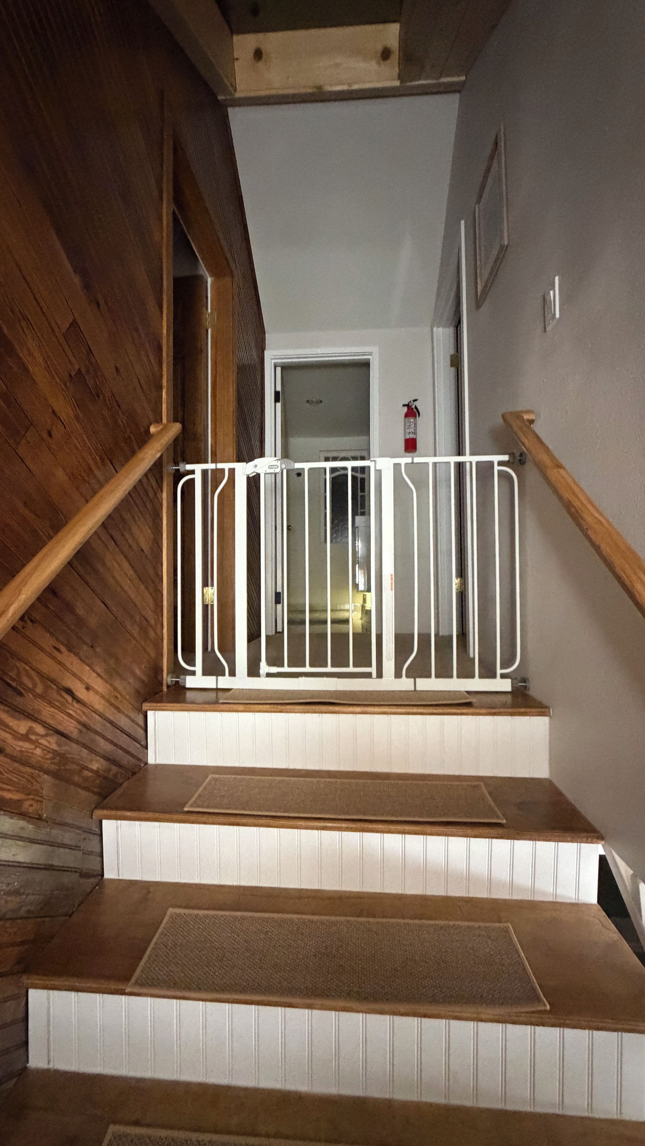A wooden staircase with a white railing and a fire extinguisher mounted on the wall.