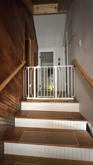 A wooden staircase with a white railing and a fire extinguisher mounted on the wall.