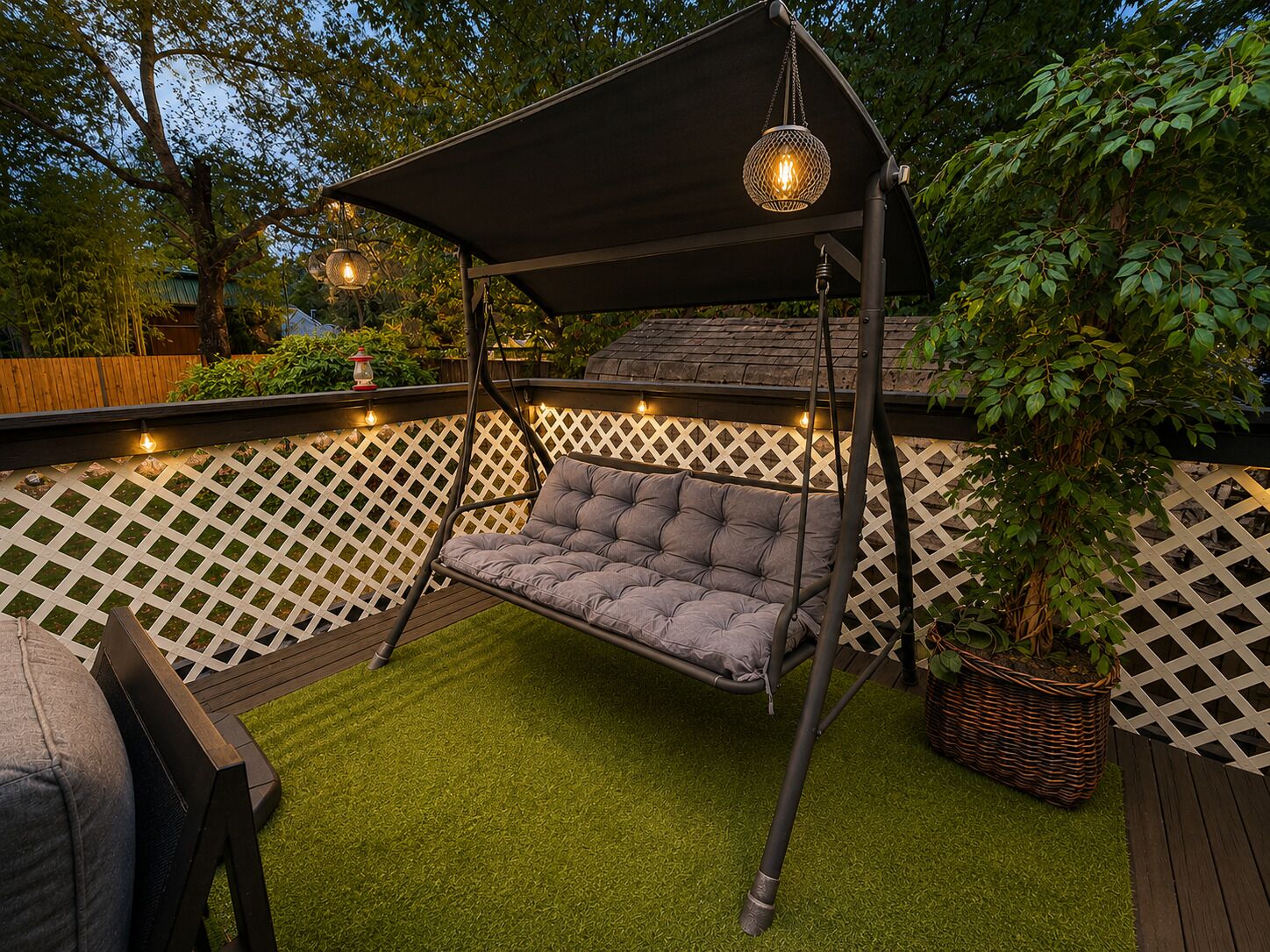 A backyard with a swing chair, artificial grass, a wooden deck, and a white lattice fence.