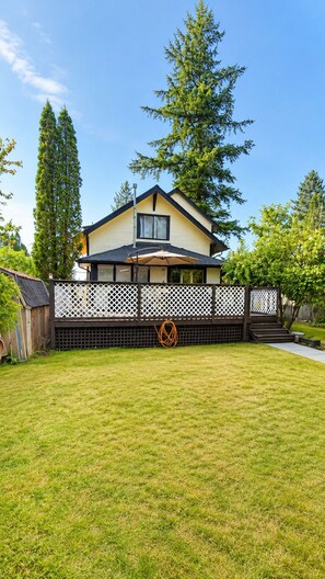 Ein zweigeschossiges Haus mit einem eingezäunten Hinterhof, einer Holzterrasse und einem Rasen.