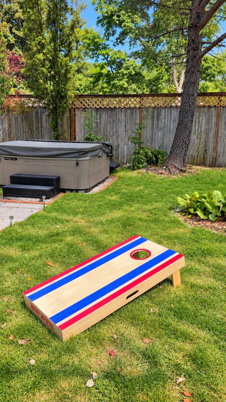 A backyard with a hot tub, a wooden deck, and a cornhole game set.