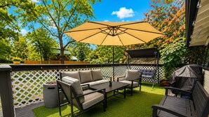 An outdoor patio with a wooden deck, a beige sofa, a table, and a barbecue grill. - Mountain Cabin With Hot Tub & Fire Pit, Wallace Falls & Stevens Pass (Gold Bar)