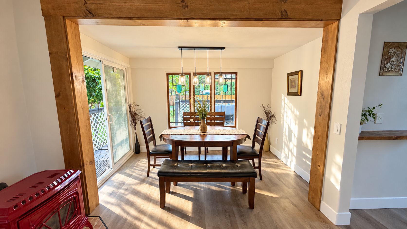 Un coin repas avec une table en bois, des chaises et un banc. Une fenêtre offre une vue sur la verdure à l’extérieur.