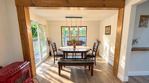 A dining area with a wooden table, chairs, and a bench. There is a window with a view of greenery outside. - Charming Farmhouse with Hot Tub, Fire Pit & Mountain Views near Wallace Falls (Gold Bar)
