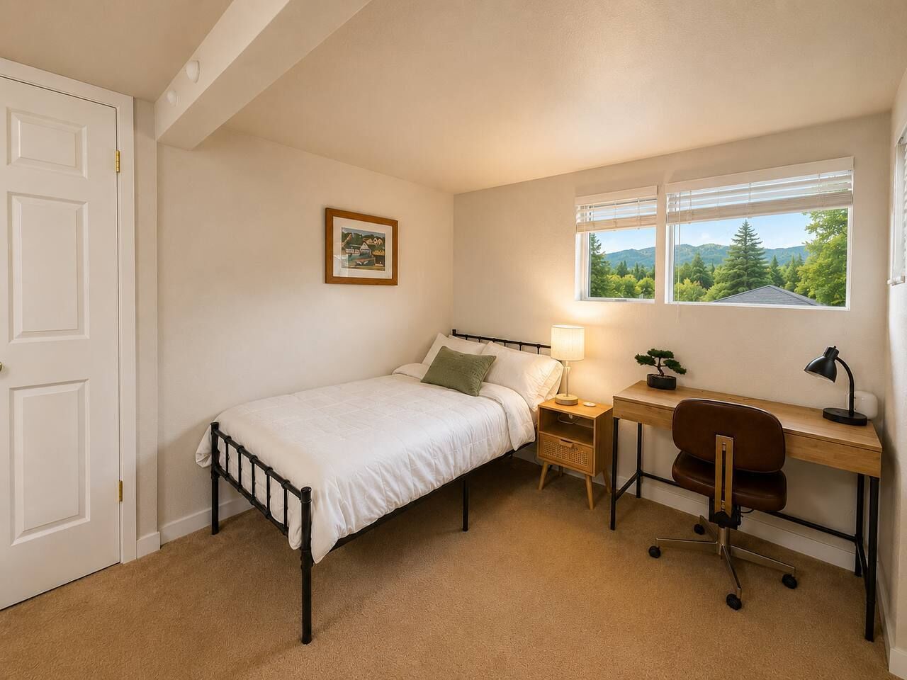 A bedroom with a single bed, a desk, a chair, a lamp, and a window with a view of trees and mountains.