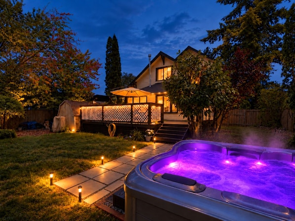 A backyard with a hot tub, a covered patio area, and a house with a visible deck.