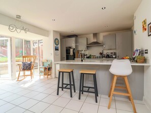 A modern kitchen with a central island, bar stools, and a dining area with a rocking chair. - Manning's View (Barnstaple)
