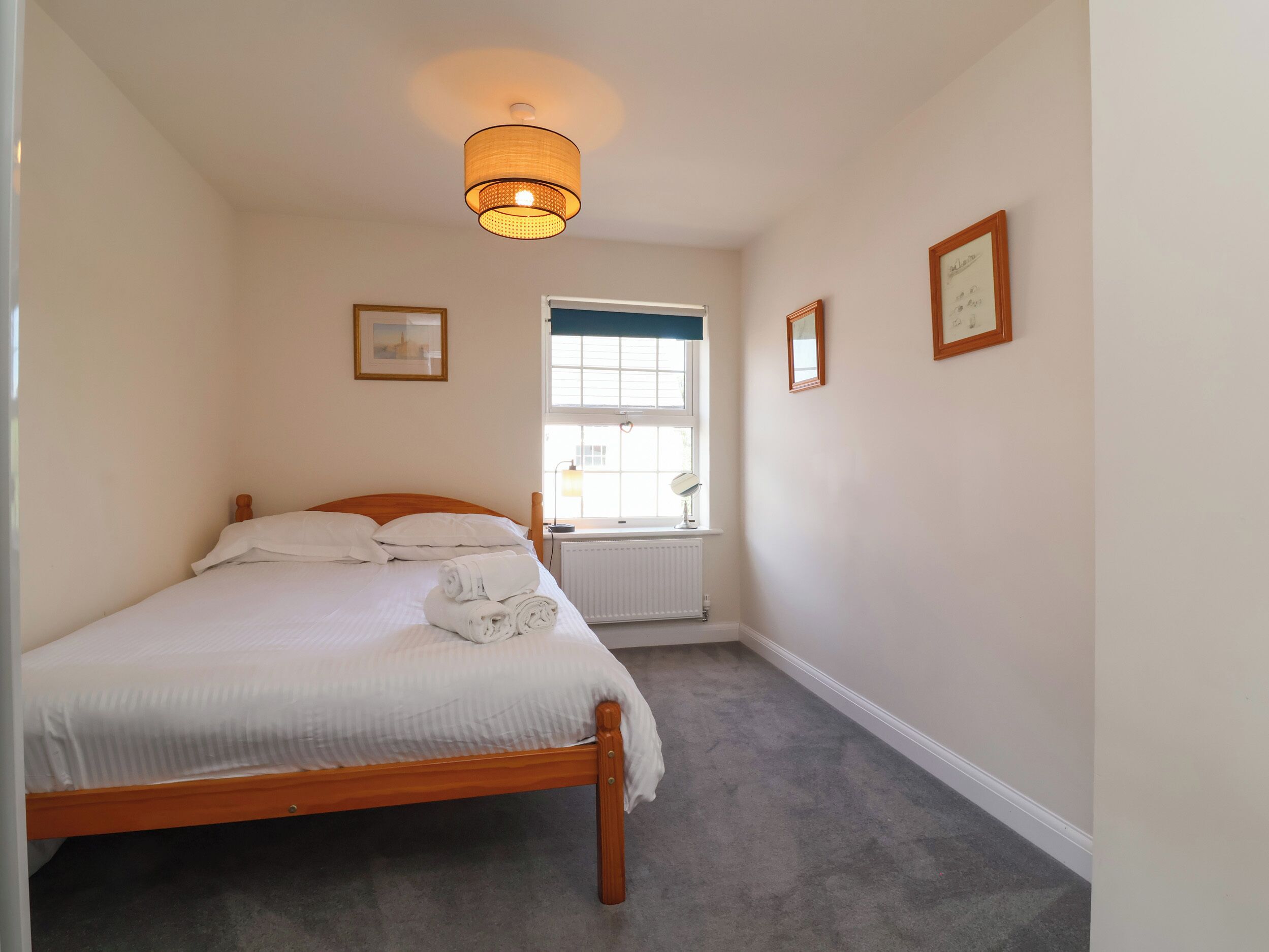 Une chambre avec un lit, une fenêtre, un radiateur et des tableaux encadrés accrochés au mur.