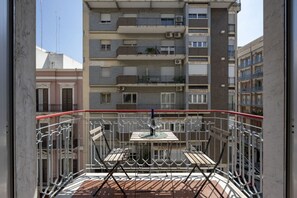 Un balcone con tavolo e sedie, affacciato su un edificio a più piani con balconi.