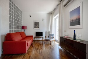 Ein Wohnzimmer mit einem roten Sofa, einem Fernseher, einem Holztisch und einem großen Fenster mit Vorhängen.