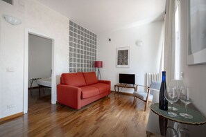 Ein Zimmer mit einem roten Sofa, einem Fernseher, einem kleinen Tisch mit Gläsern und einer Heizung.