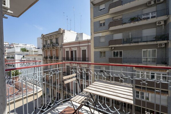Un balcone con ringhiera in metallo, un tavolo di legno e vista su edifici vicini.