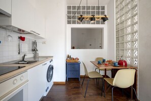 Uma cozinha compacta com máquina de lavar, uma área de refeições com mesa e cadeiras, e uma janela com vista.