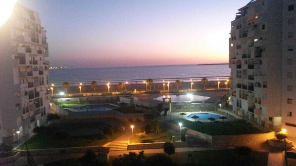 A residential complex with multiple swimming pools, a view of the sea, and a well-lit promenade.