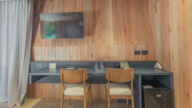 A modern room with a wooden wall, a flat-screen TV, a desk with two chairs, and a minibar. - Locus Solus Hotel Singular (Mar del Plata)