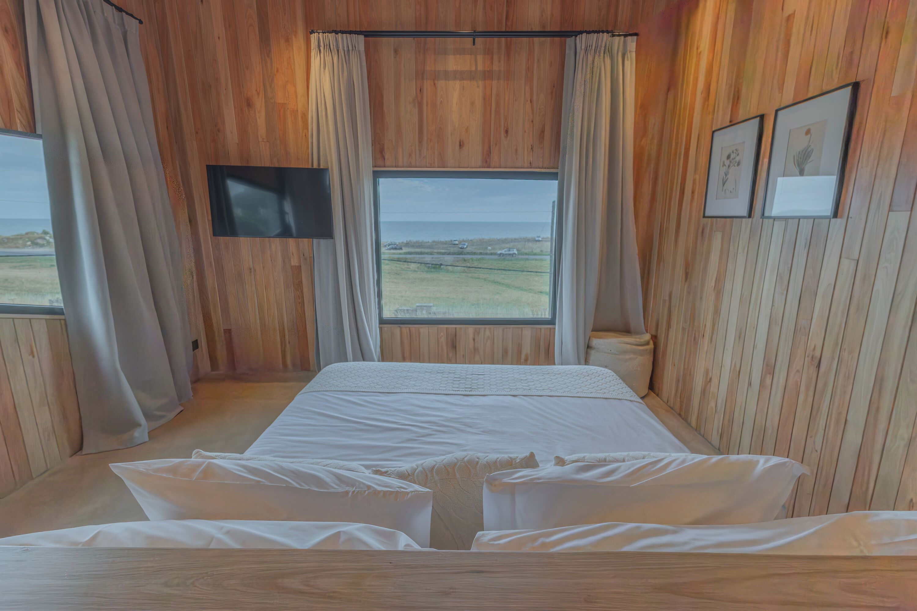 A room with a bed, a television, and a window with a view of the beach.