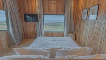 A room with a bed, a television, and a window with a view of the beach.