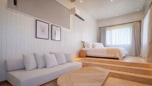 A modern bedroom with a bed, a sofa, and a small table. There are stairs leading to the bed, and the room has a minimalist design with white walls and a wooden floor. - Locus Solus Hotel Singular (Mar del Plata)