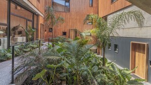 A modern building with wooden exterior walls, large windows, and a courtyard with various plants. - Locus Solus Hotel Singular (Mar del Plata)
