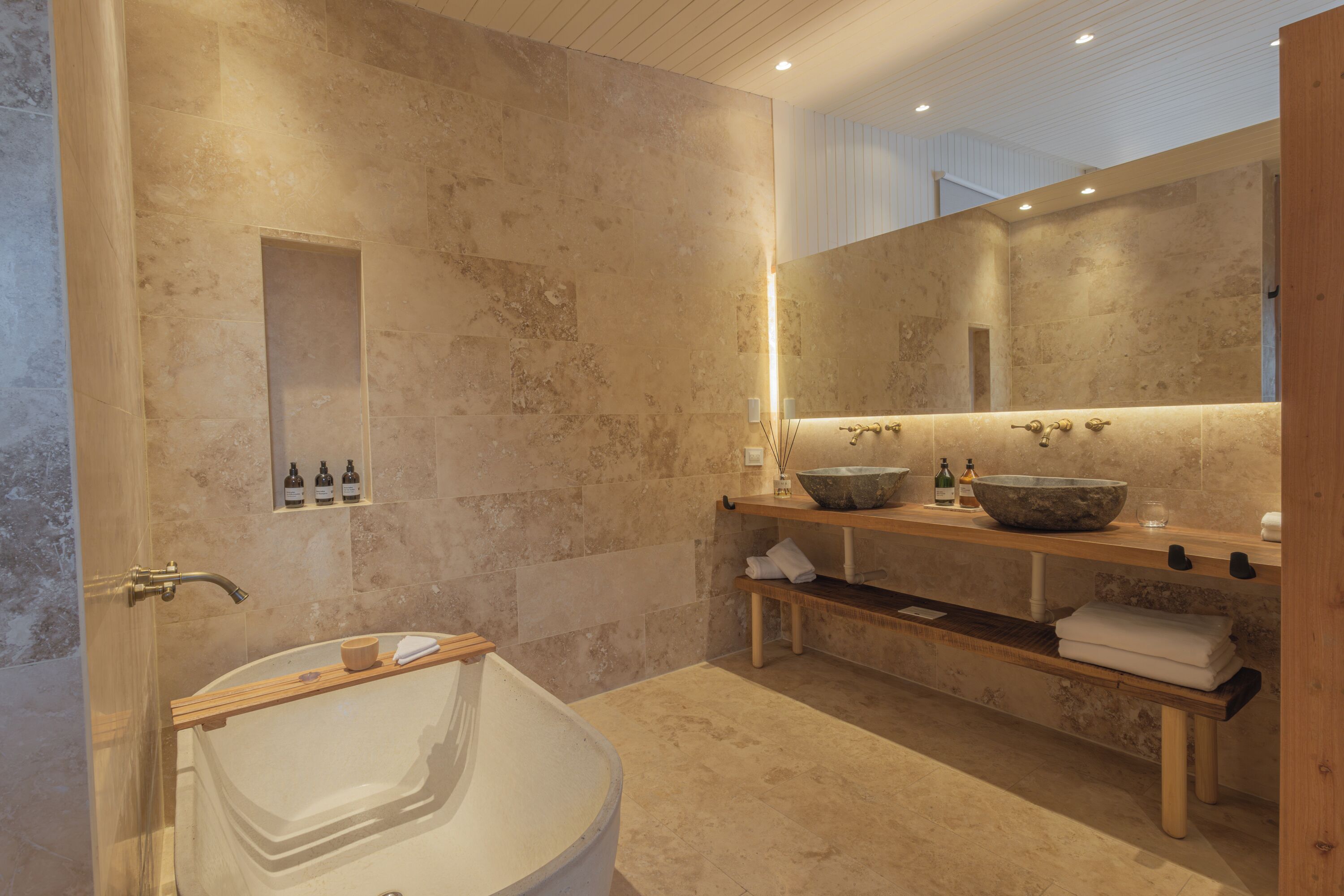Un baño moderno con una bañera independiente, un espejo grande y un mueble de tocador de madera con lavabo de piedra.