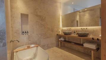 Un baño moderno con una bañera independiente, un espejo grande y un mueble de tocador de madera con lavabo de piedra.