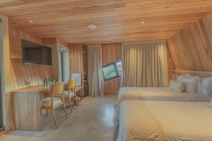 A hotel room with a wooden ceiling, a desk with chairs, a bed, and a television mounted on the wall.