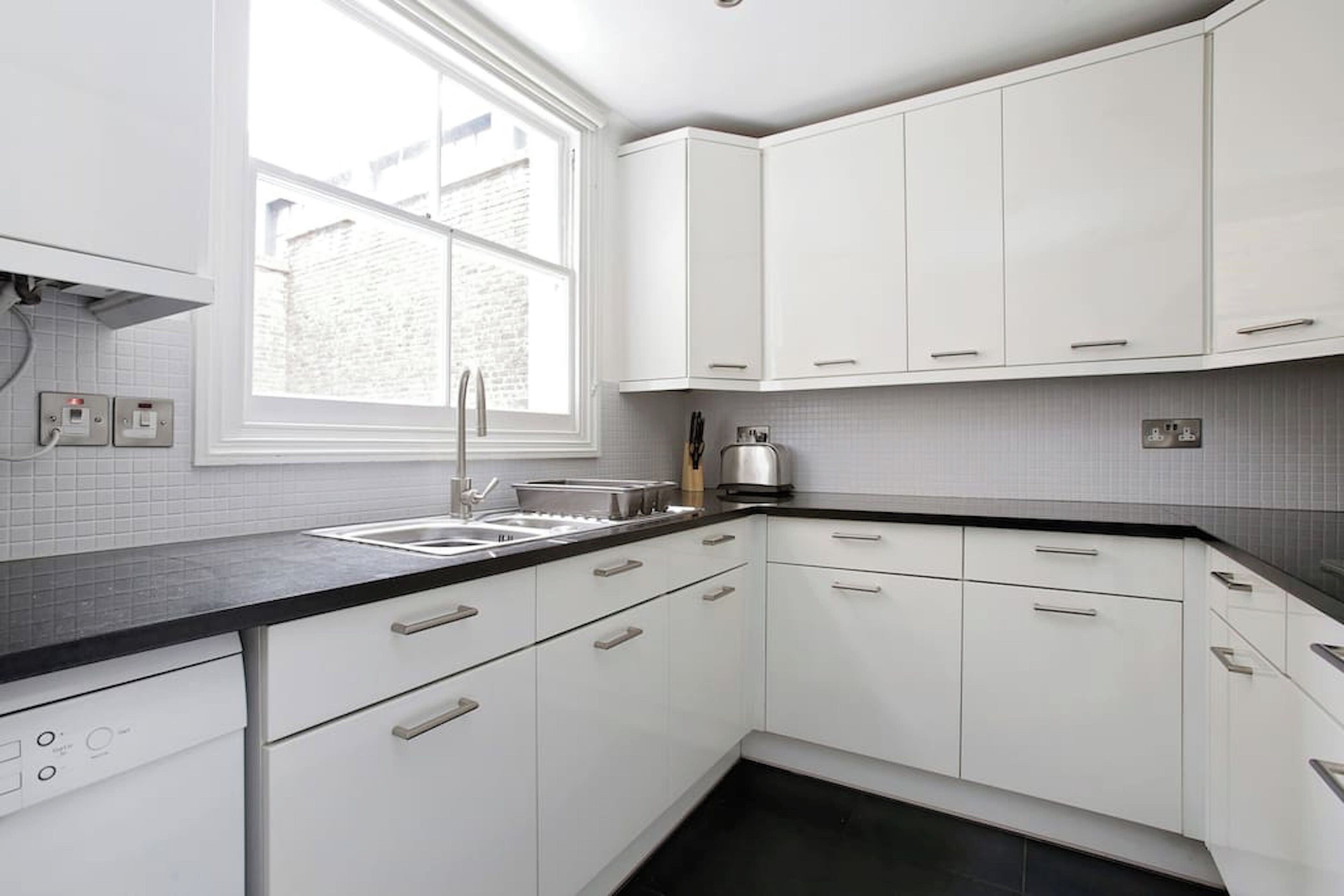 A modern kitchen with white cabinets, a black countertop, and a window providing natural light.