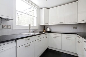 Cocina moderna con armarios blancos, encimera negra y ventana que deja entrar luz natural.