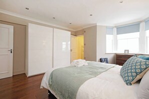 Un dormitorio con cama, armario, ventana y mesita de noche.